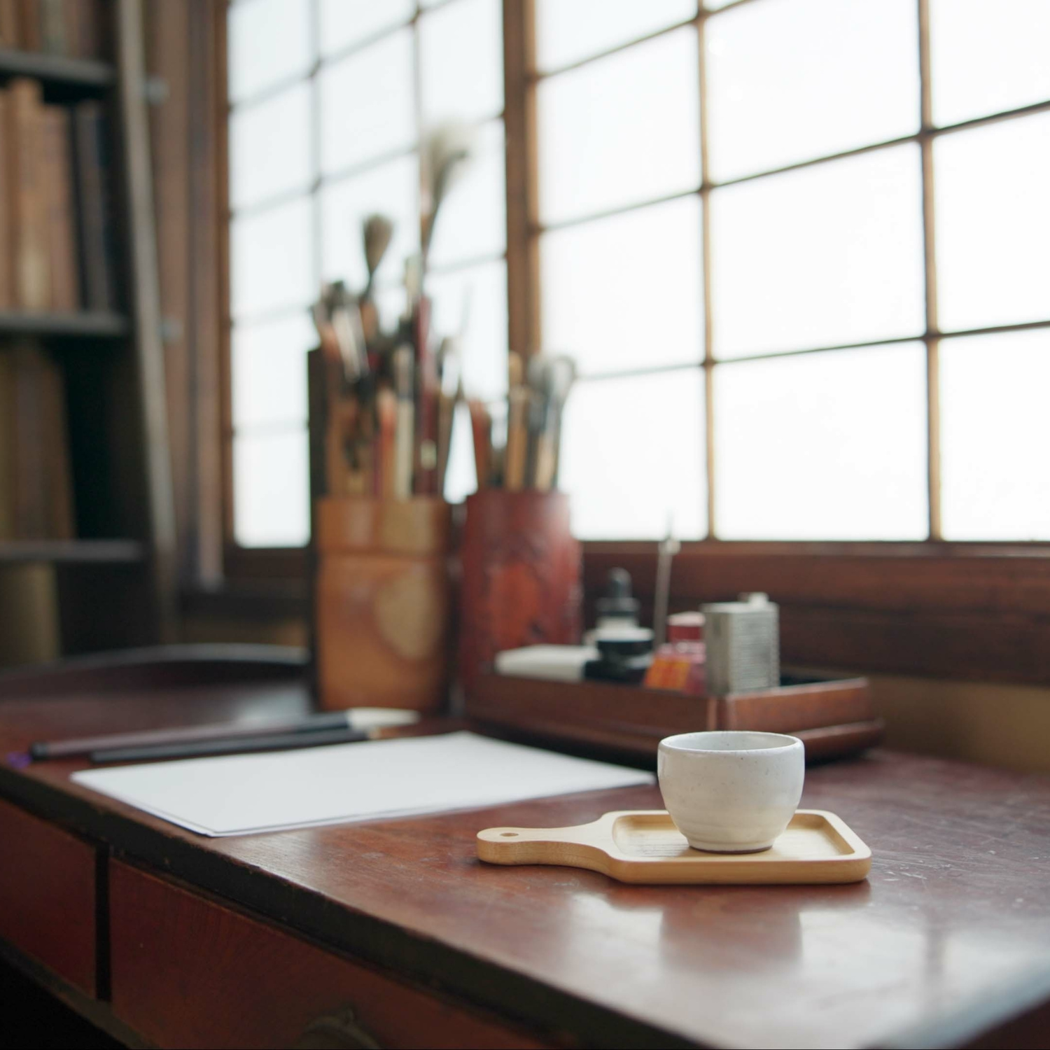 Ceramic cup on a wooden tray with brushes and art supplies in the background. to illustrate book from Fern Jean-Joseph