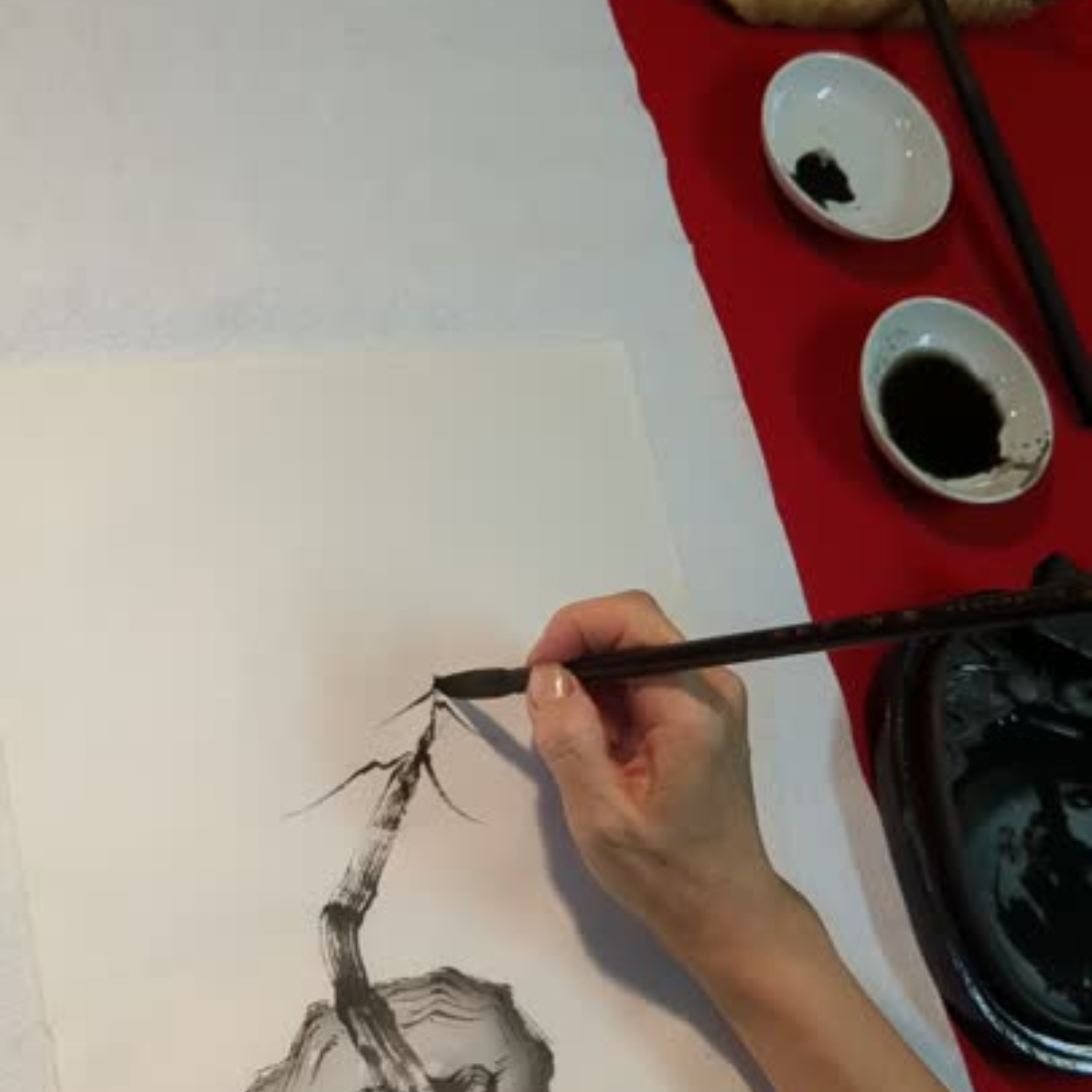 Harumi Kobayashi  painting  a sumi-e art piece on paper with a brush, ink stones, and inkwell in the background.