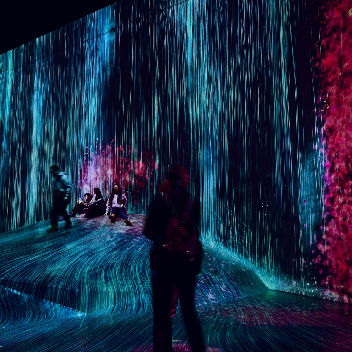 People interacting with a digital art installation featuring colorful light projections.